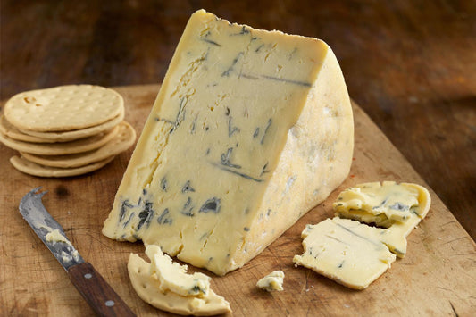 A wedge of Beauvale Blue Cheese on a wooden cutting board next to some crackers 