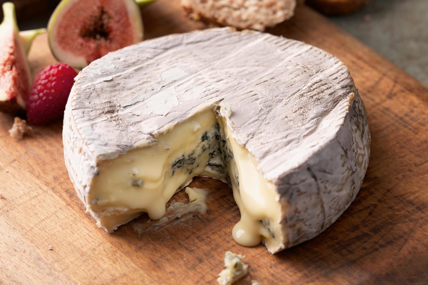 Cote Hill Blue Cheese Wheel with a wedge cut out next to a raspberry and a fig on a wooden serving board  